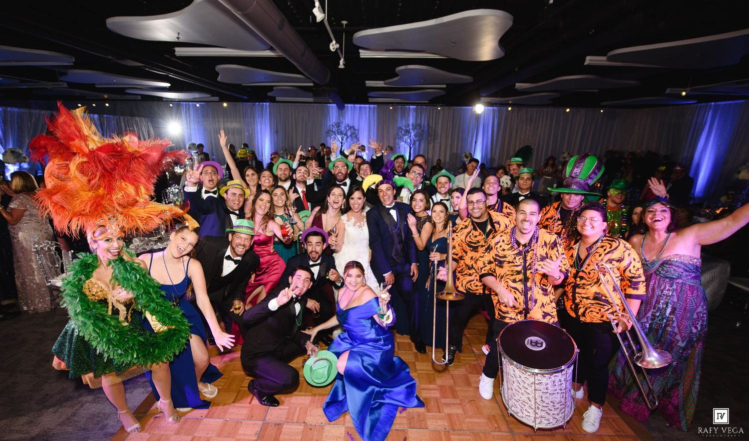 Colorful masquerade party with costumed guests posing together on a dance floor with vibrant decorations.