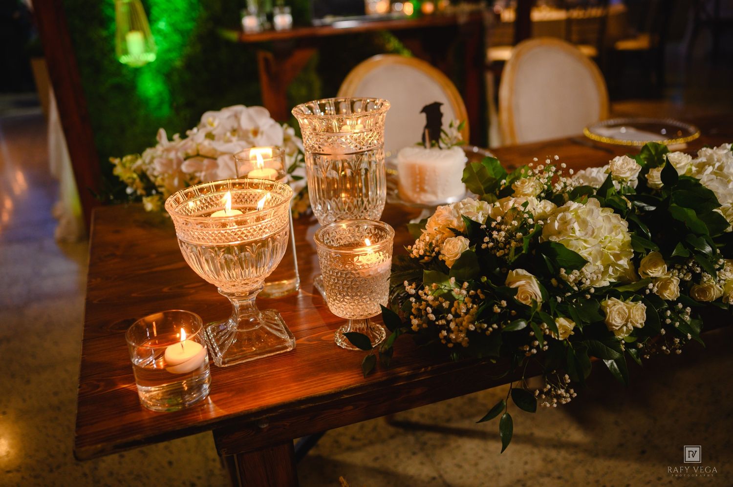 Elegant wedding table centerpiece with crystal candle holders, white floral arrangement, and a small wedding cake topper.