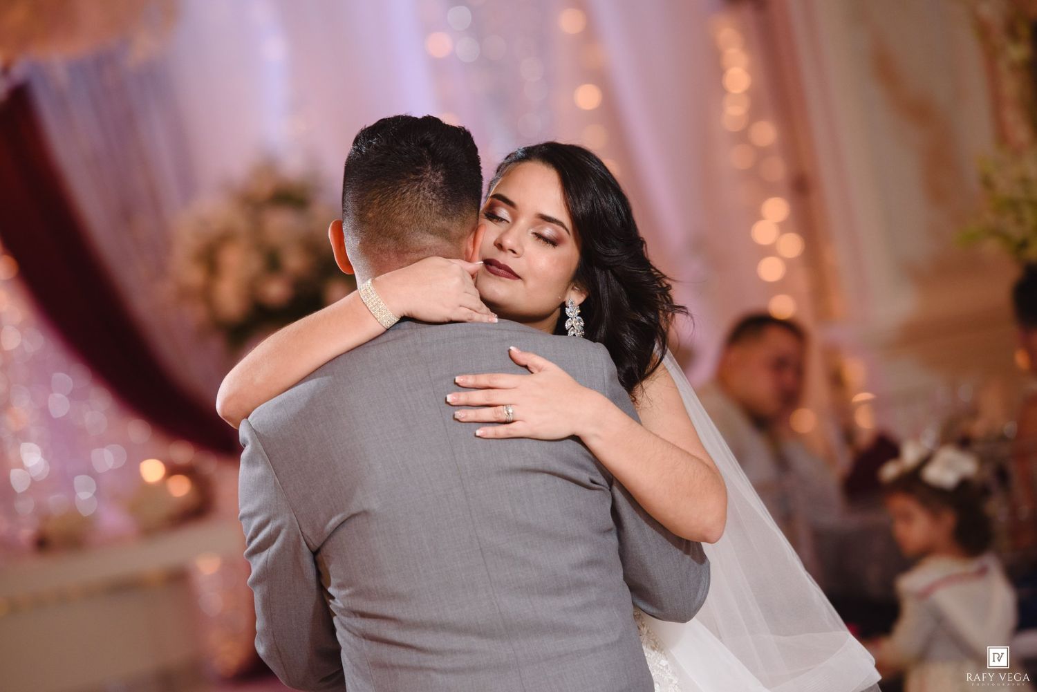 Bride and groom share an emotional first dance embrace at elegant wedding reception with floral decorations.
