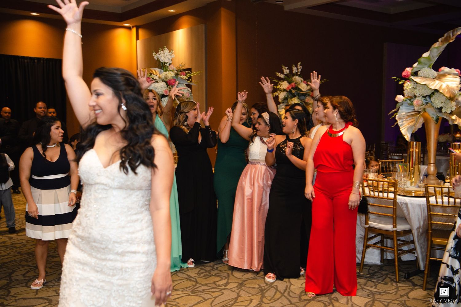 Bride tossing bouquet to excited bridesmaids in colorful gowns at elegant wedding reception.