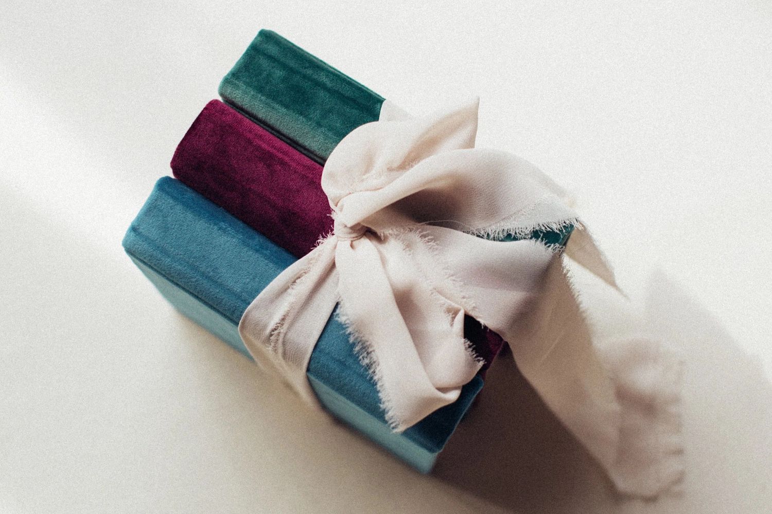 Elegant gift wrapped in teal and burgundy velvet fabric tied with a white satin bow on a white surface.