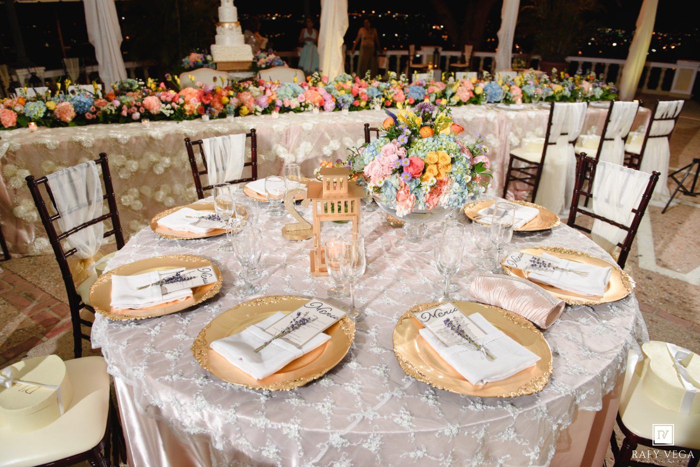 Elegant wedding reception table set with gold chargers, floral centerpiece, and white lace tablecloth.