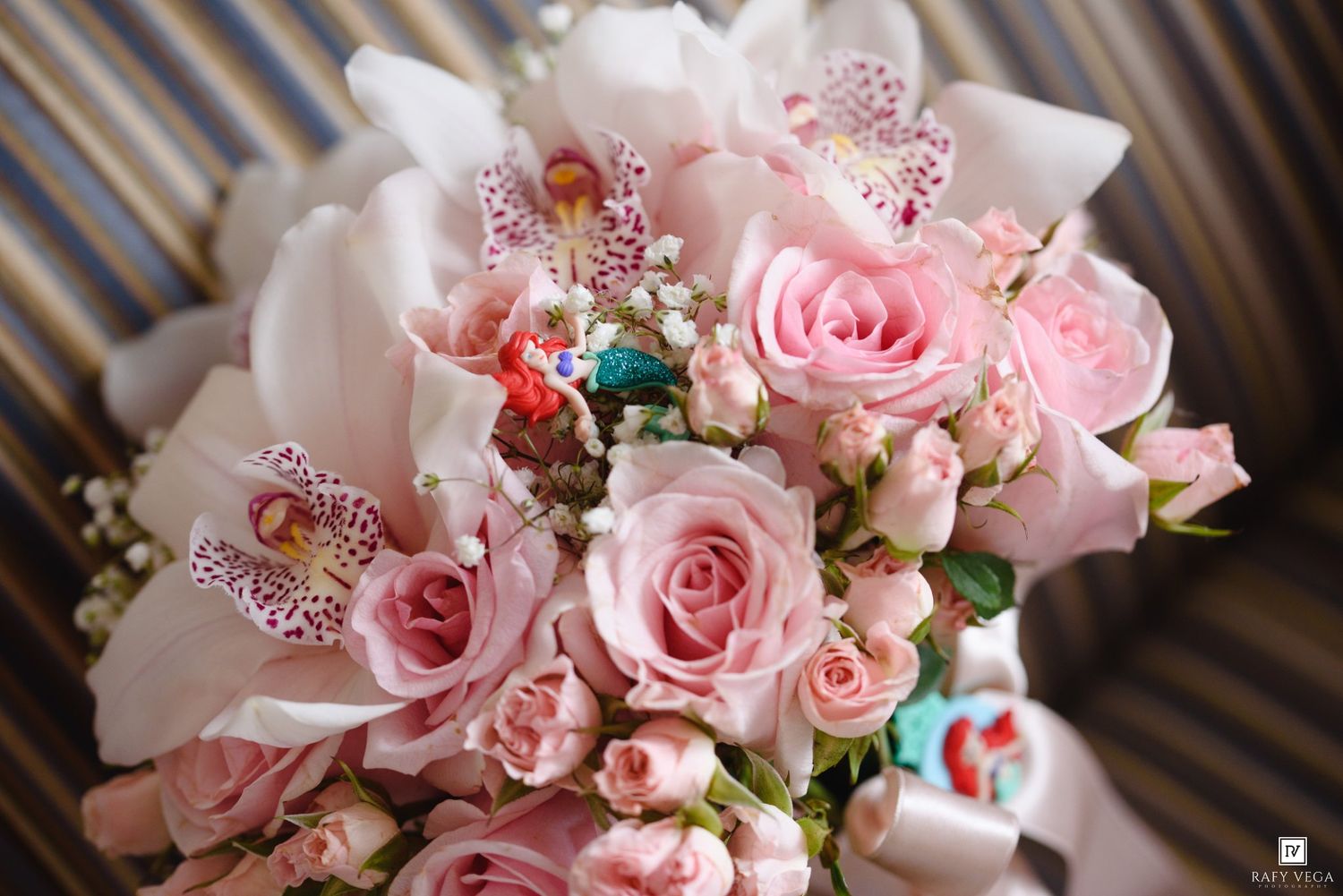 A bridal bouquet of pink roses and white orchids with decorative accents arranged on a striped background.