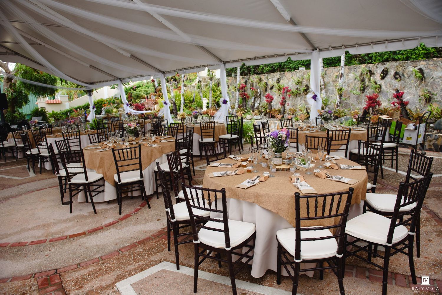 Elegant outdoor wedding reception under a white tent with round tables, chiavari chairs, and floral centerpieces.
