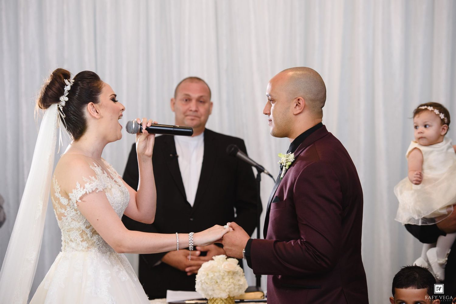 Bride singing vows into microphone while groom holds hands at elegant wedding ceremony altar.
