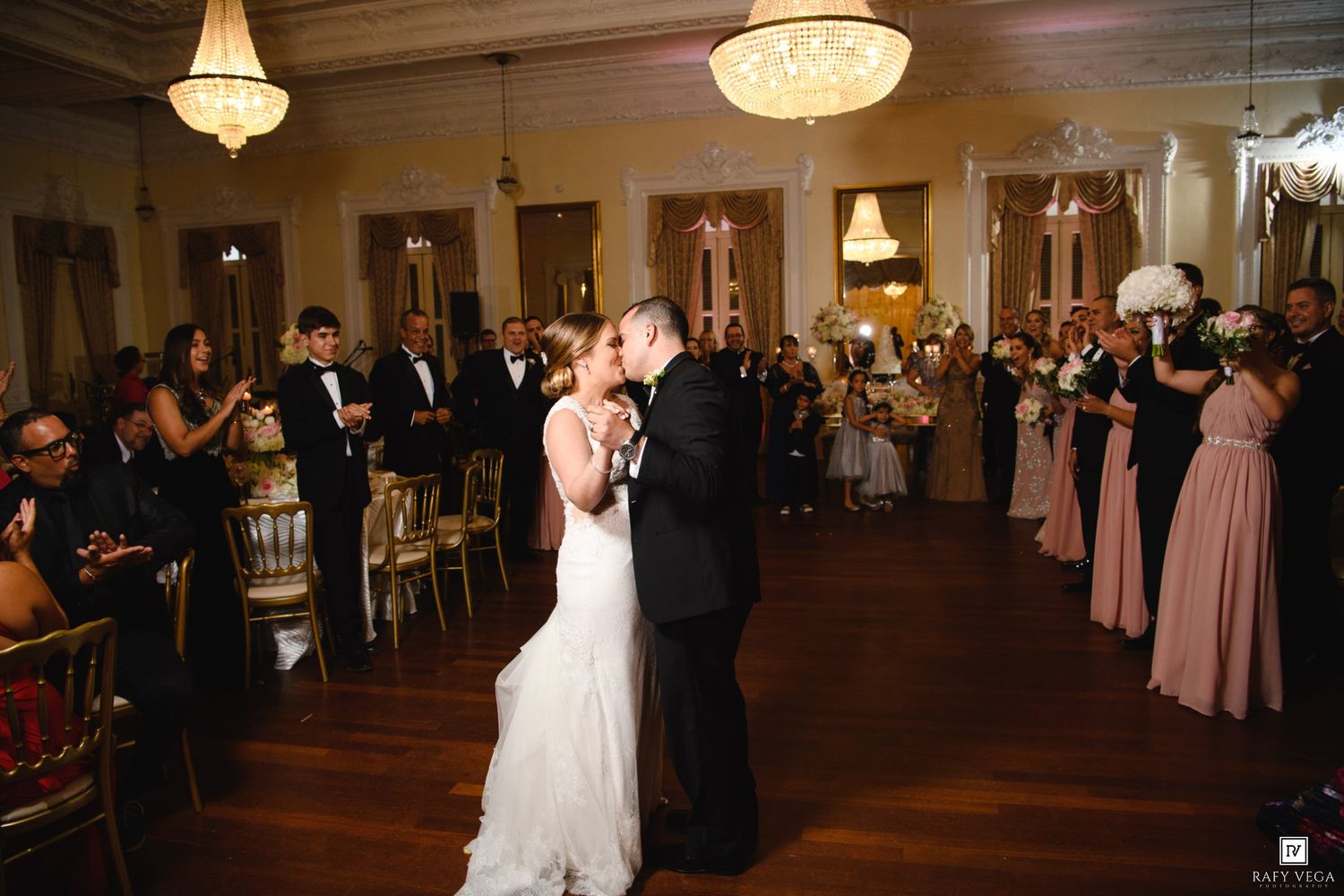 Bride and groom share first dance surrounded by guests in elegant ballroom wedding reception.