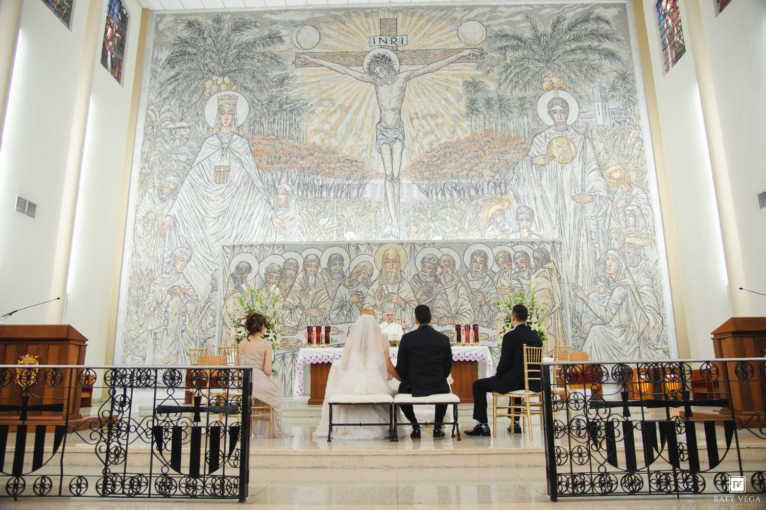 Wedding couple kneels at altar beneath stunning mosaic mural during church ceremony.