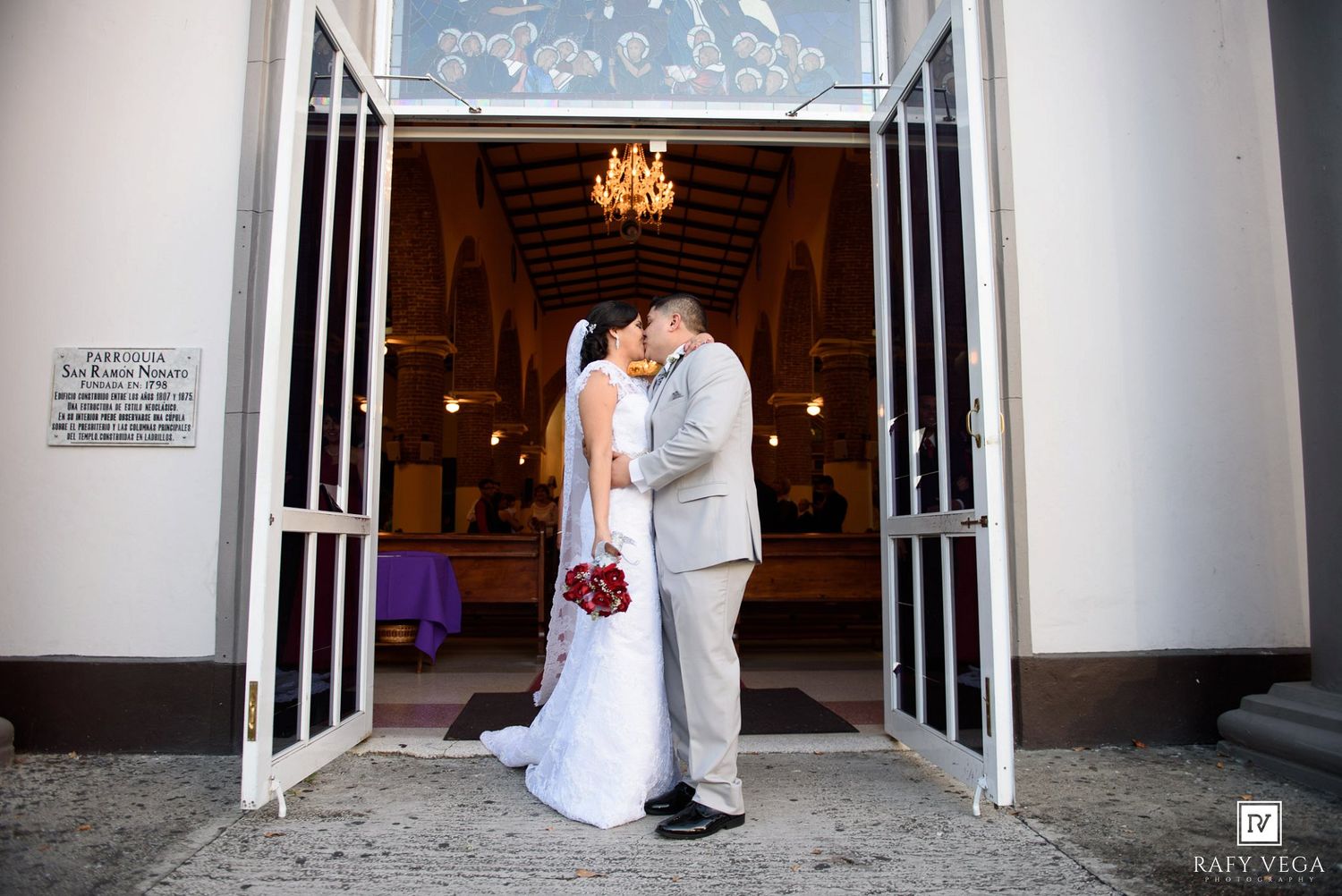 Bride and groom sharing a kiss at the entrance of a decorated Catholic church after their wedding.