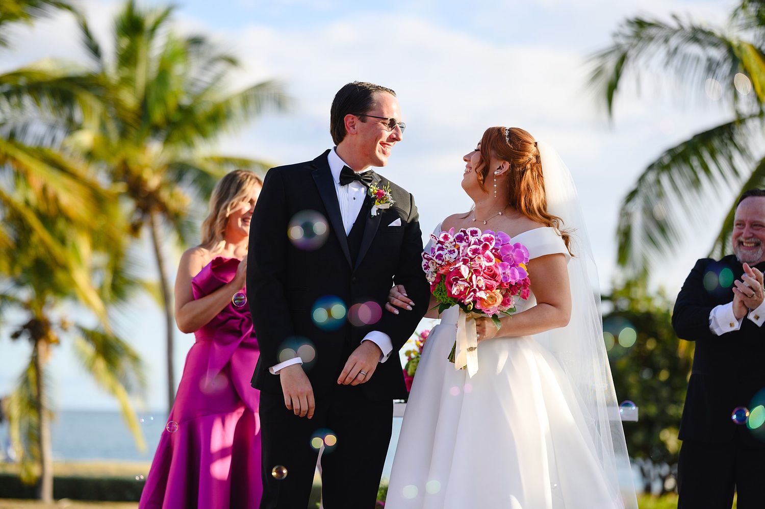 Newlyweds share a joyful moment surrounded by bubbles at a tropical outdoor wedding.