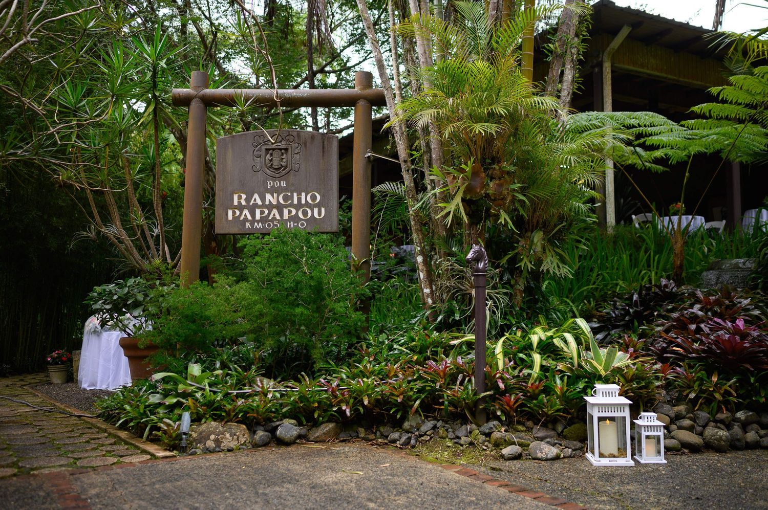 Rancho Papapou entrance sign surrounded by lush tropical greenery and plants in a garden setting.