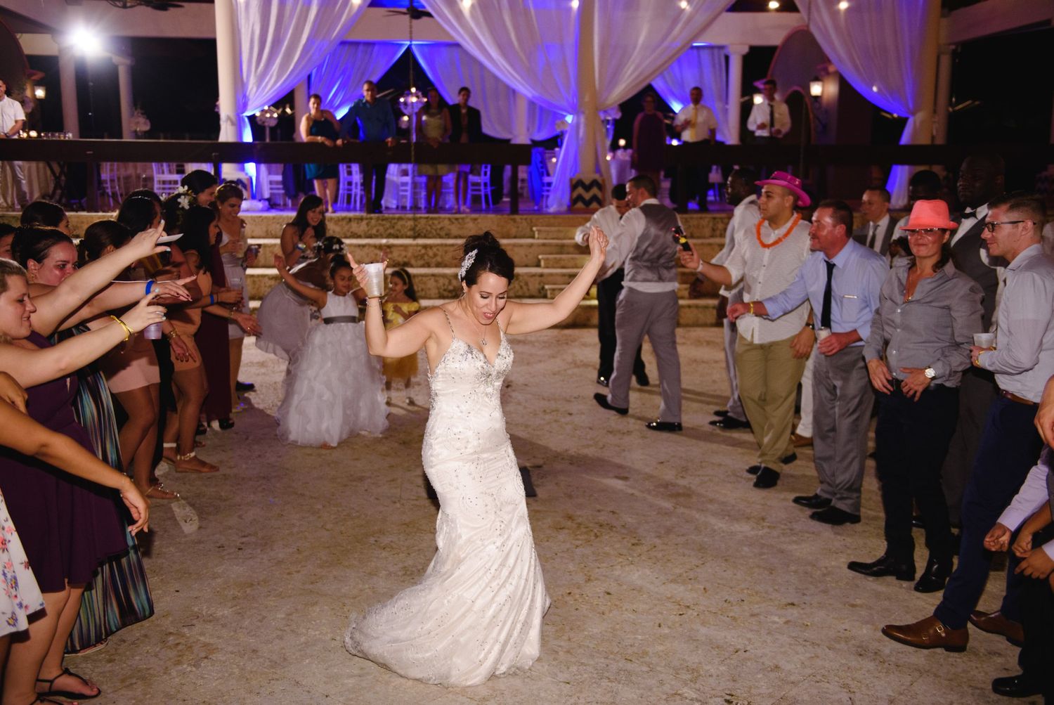Bride in white wedding gown dancing joyfully surrounded by guests at an elegant outdoor wedding reception.