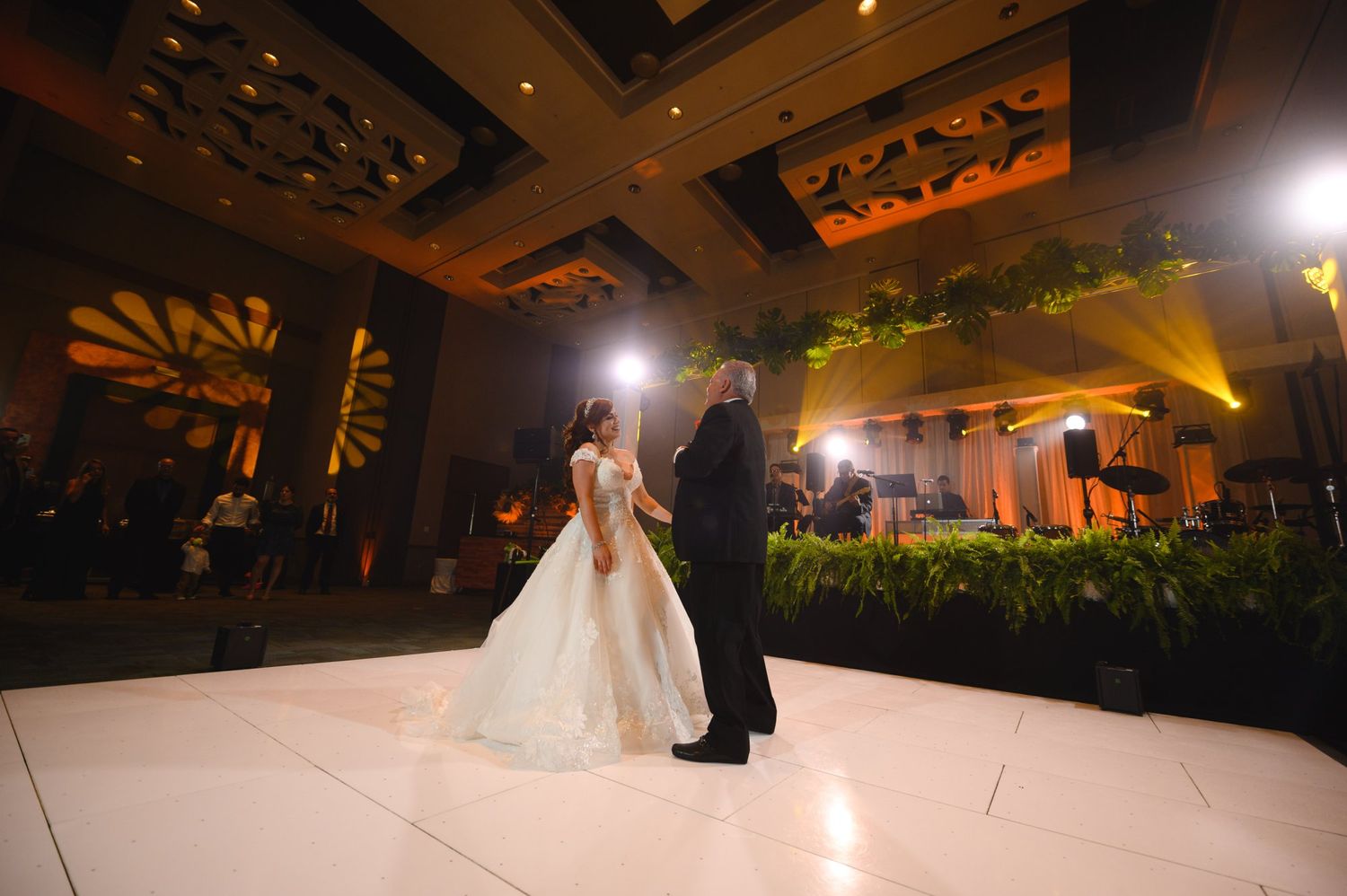 Bride and groom share their first dance on a white dance floor in an elegant ballroom wedding reception.