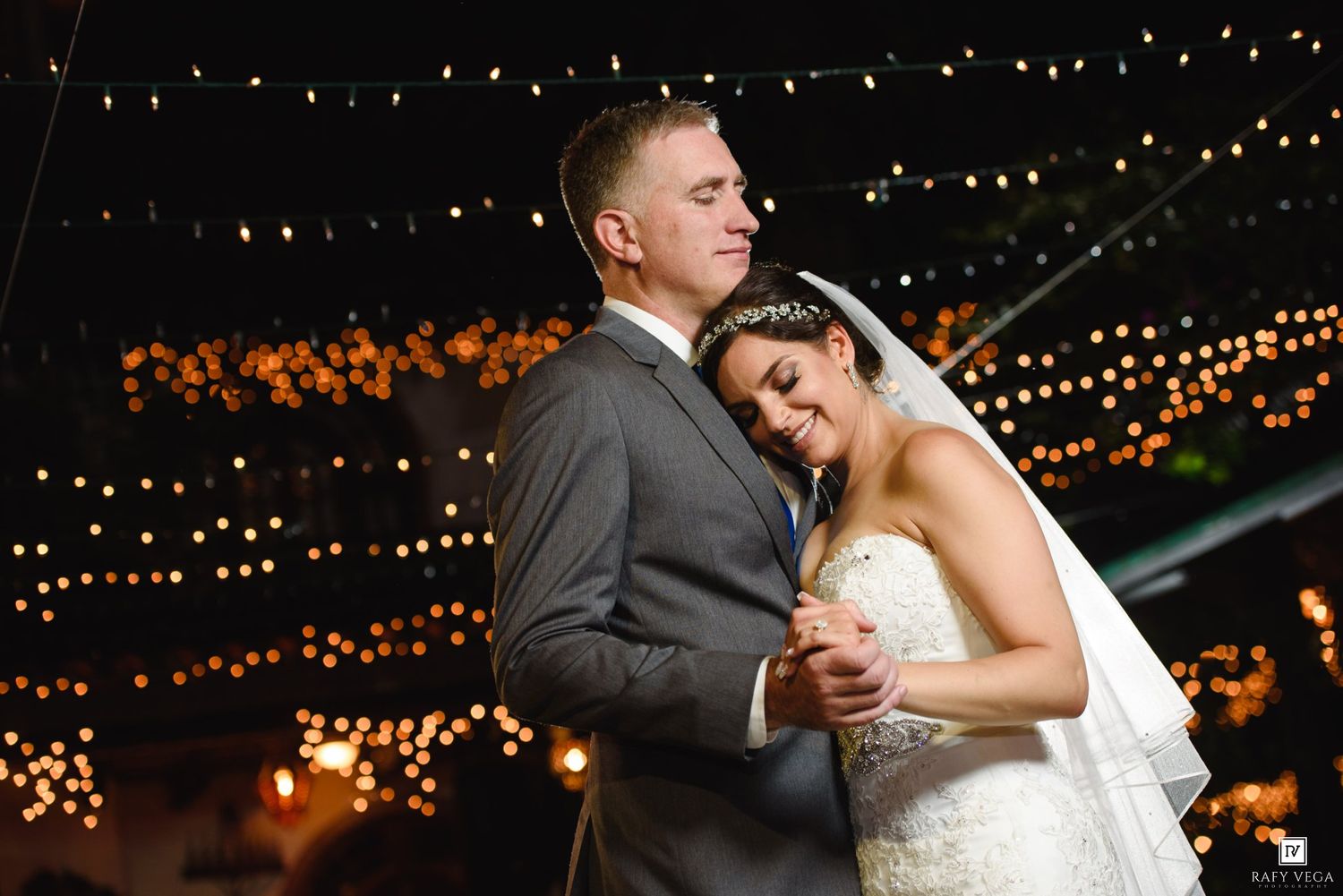Bride and groom share a romantic embrace at night, surrounded by sparkling bokeh lights at their wedding reception.