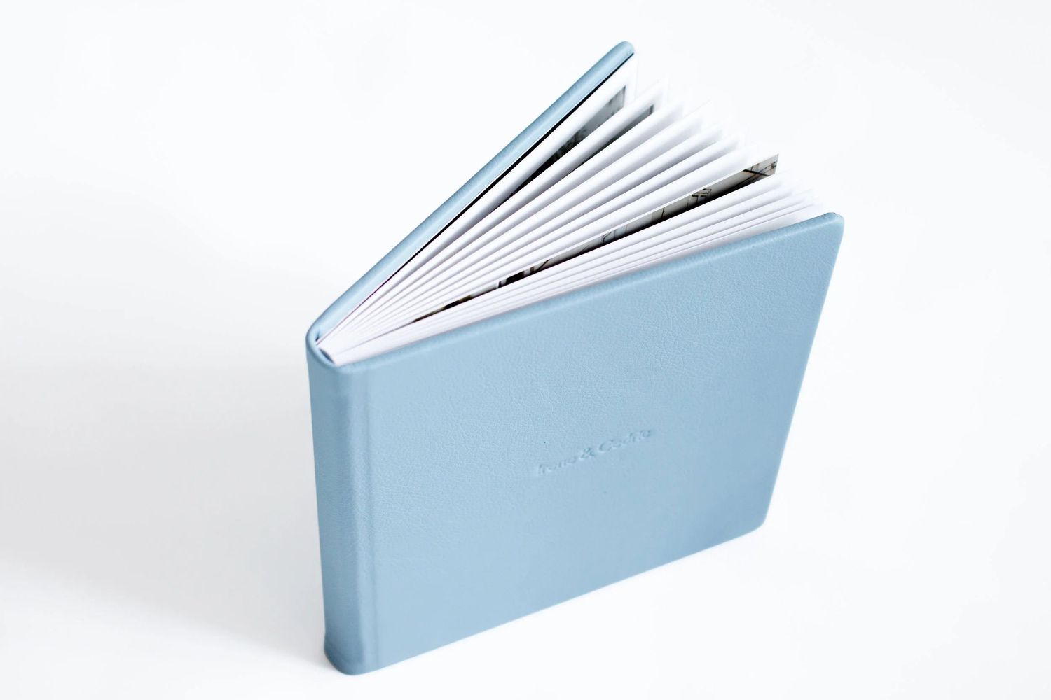 Light blue hardcover photo album open and standing upright, showing white pages, on a white background.