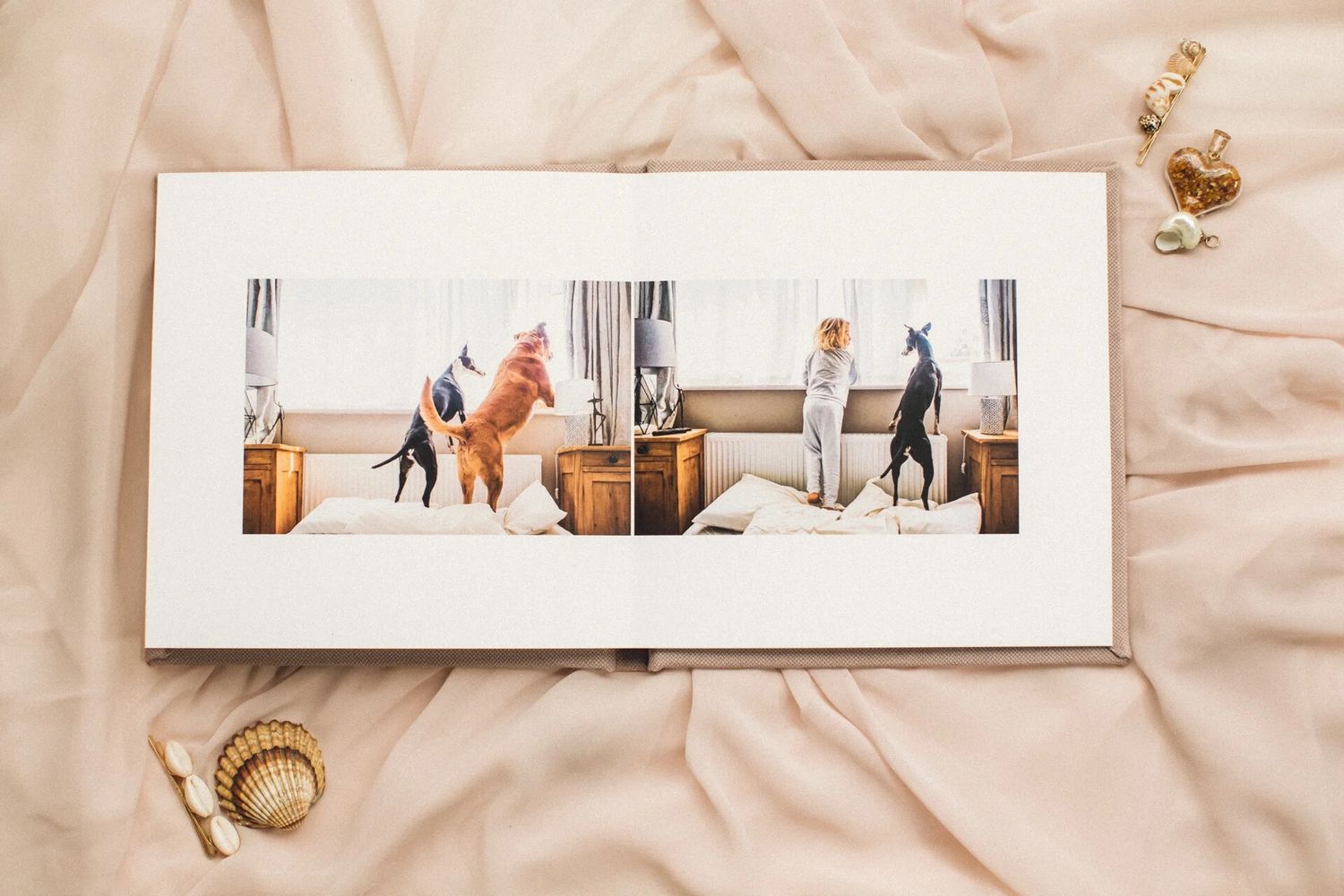 Open photo book on pink fabric displaying a panoramic image of dogs and a person in a bright room.