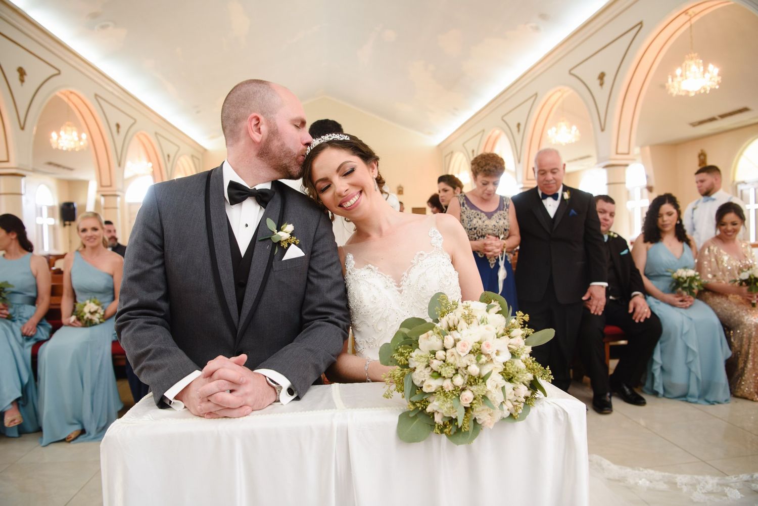 Bride and groom share a tender kiss at the altar during their elegant wedding ceremony with guests seated behind them.