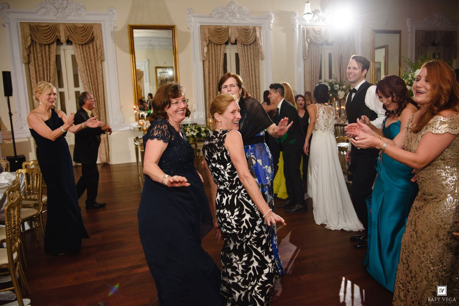 Women in formal gowns dancing and celebrating at a wedding reception party.