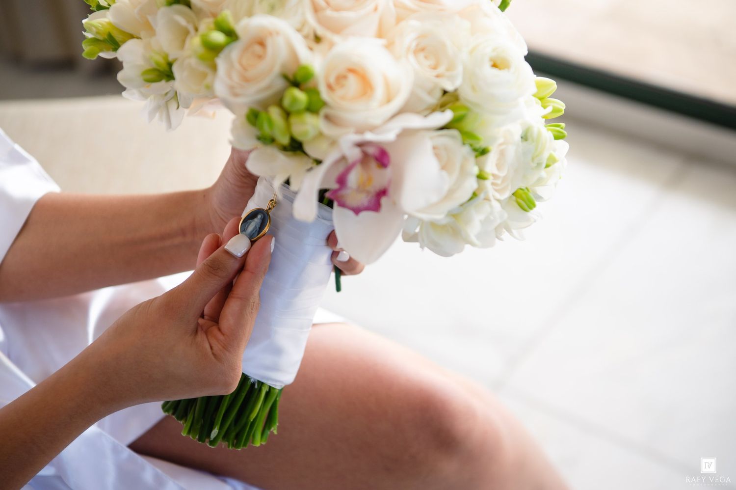 Bride holding a white wedding bouquet with roses and orchids, wrapped in white ribbon.