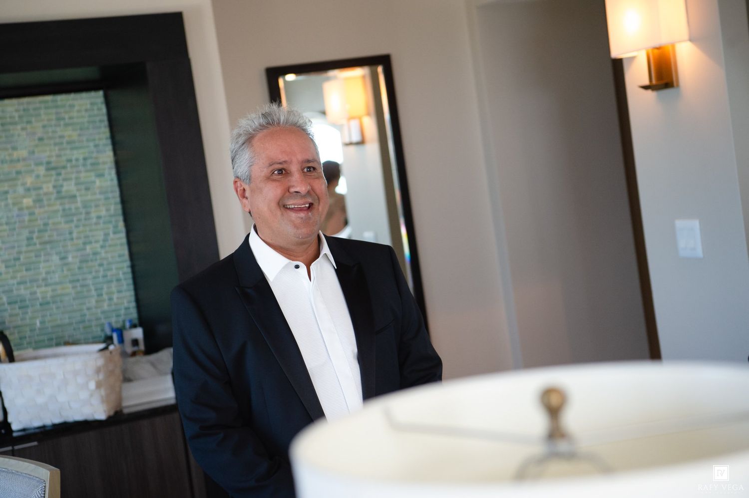 Smiling middle-aged man in navy blazer and white shirt standing in a modern, elegantly lit interior space.