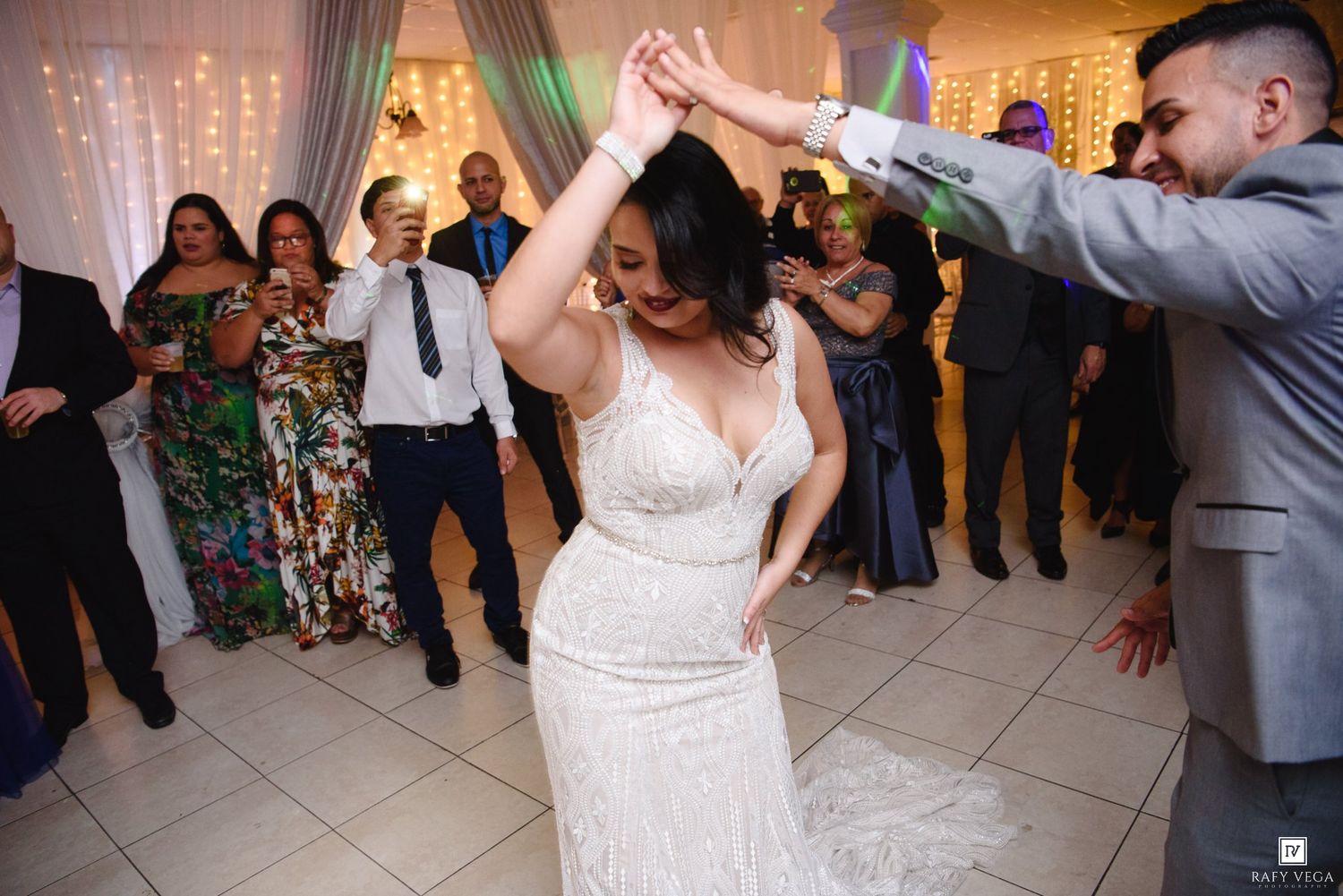 Bride in white lace gown twirling on dance floor with groom in gray suit at elegant wedding reception.