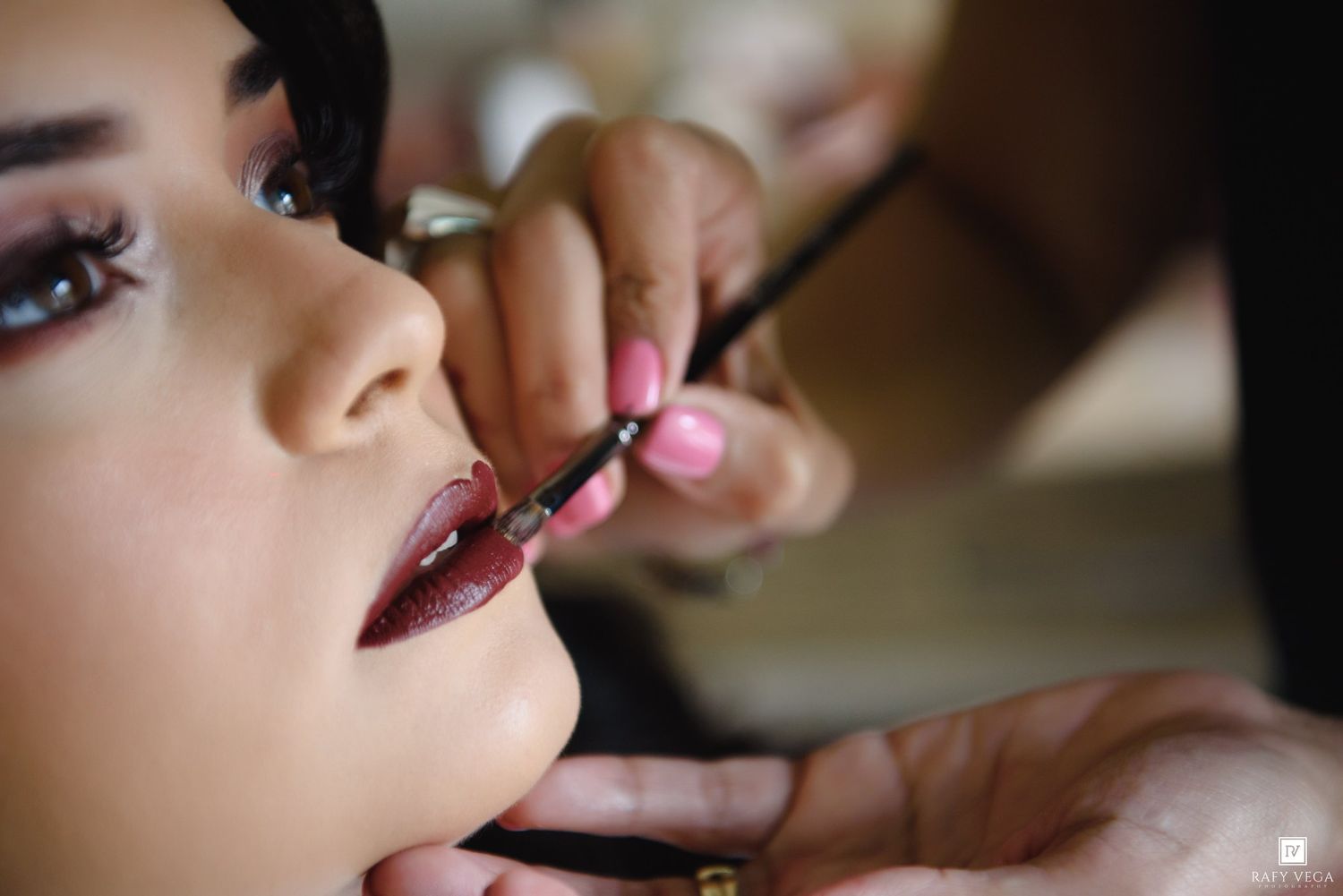 Makeup artist applying dark lip liner to a young woman with dramatic eye makeup and long lashes.
