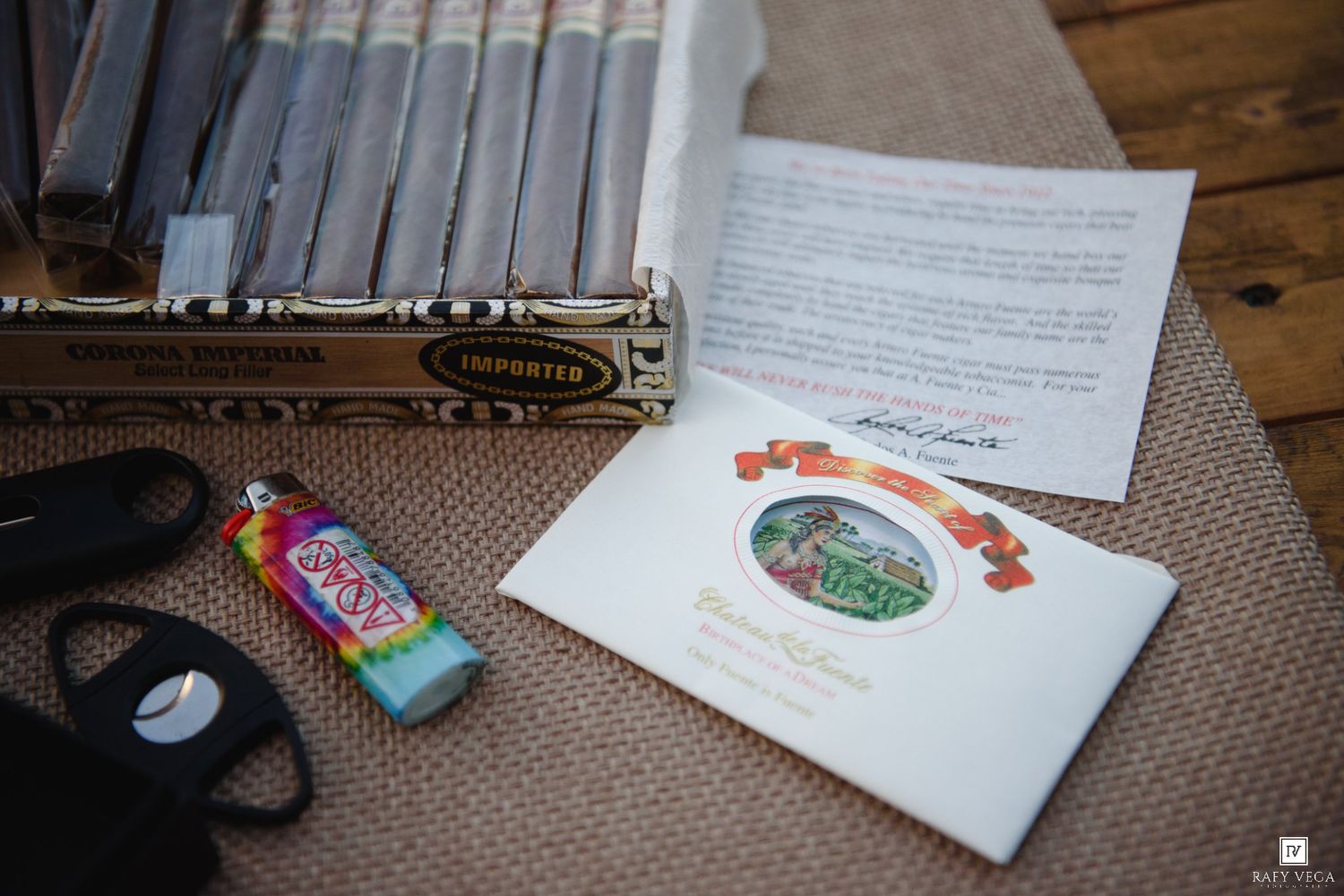 Wedding cigar bar setup with cigars, lighter, cutter, and personalized program cards on burlap table.