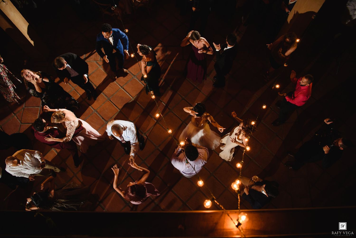 Aerial view of wedding guests dancing by candlelight on a dark wooden dance floor.