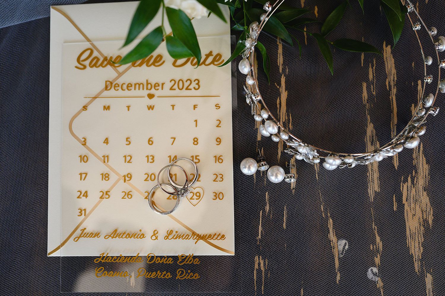 Gold laser-cut Save the Date card for December 2023 wedding in Puerto Rico, with rings and pearl bracelet on wood.