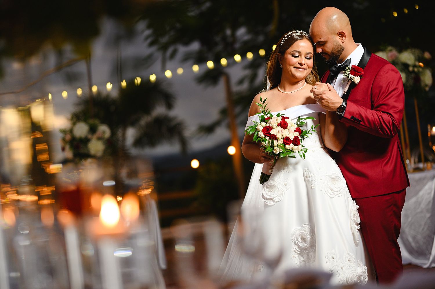 Bride and groom share a romantic first dance outdoors at an evening wedding reception with string lights.