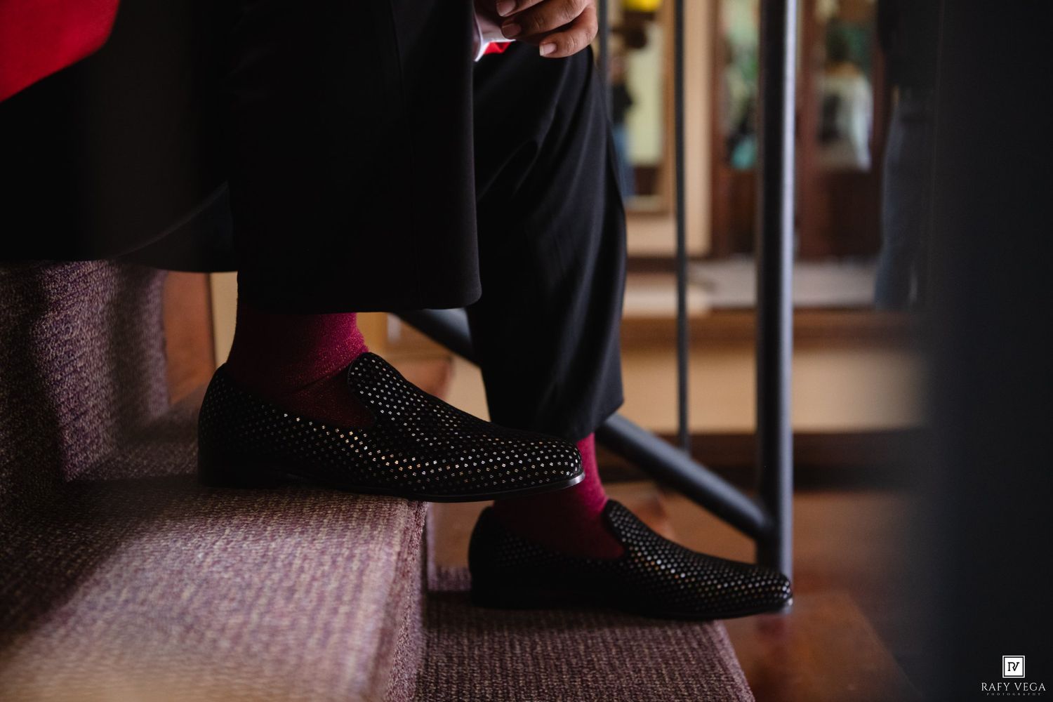Man wearing red socks and black studded loafers on wooden stairs, elegant formal attire detail shot.