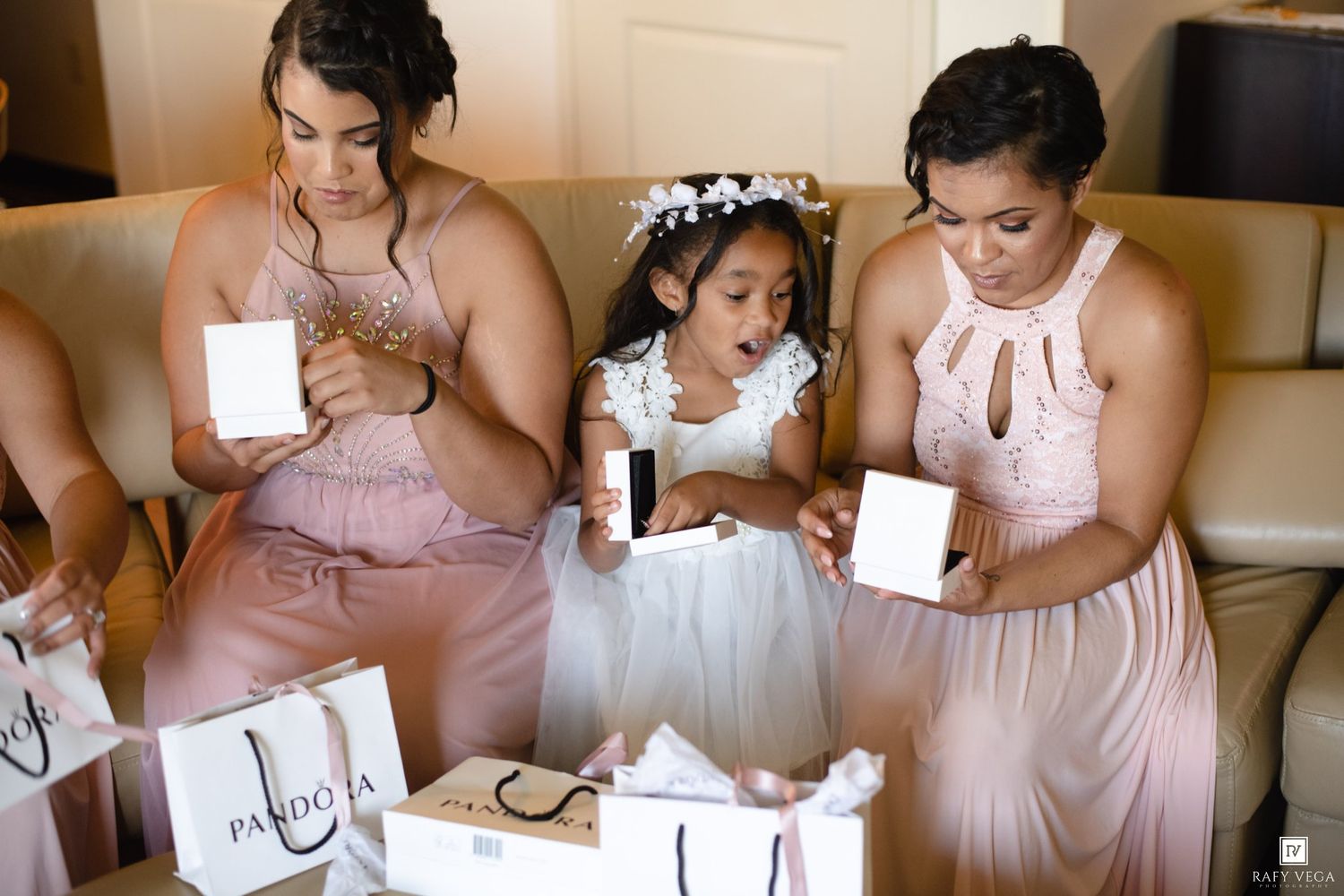 Bridesmaids and flower girl opening Pandora gift boxes at a wedding preparation, wearing pink dresses.