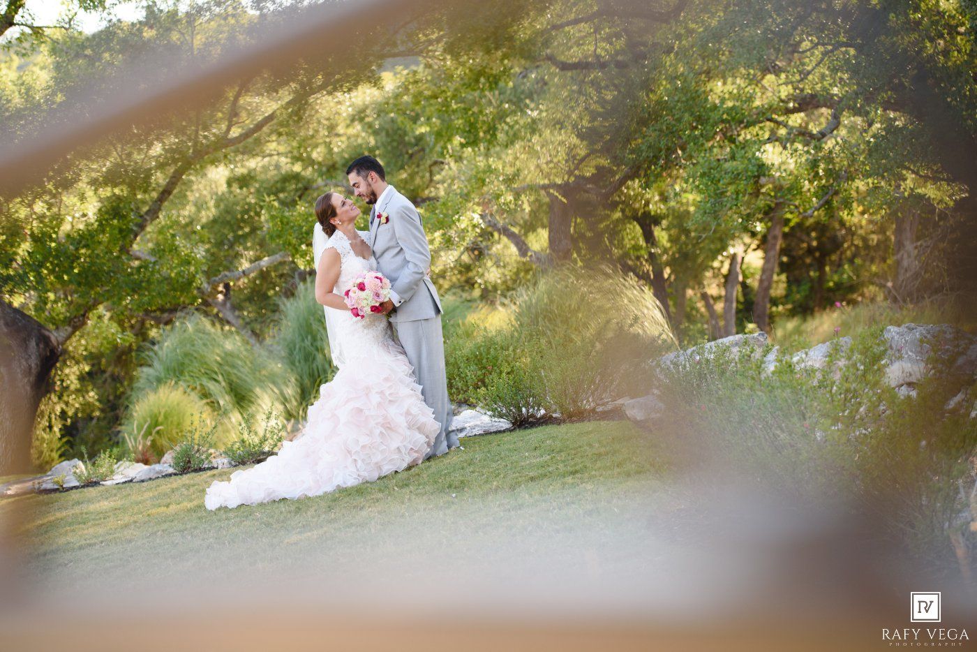 Bride and groom share romantic kiss in lush garden setting, bride wearing elegant ruffled white wedding gown.