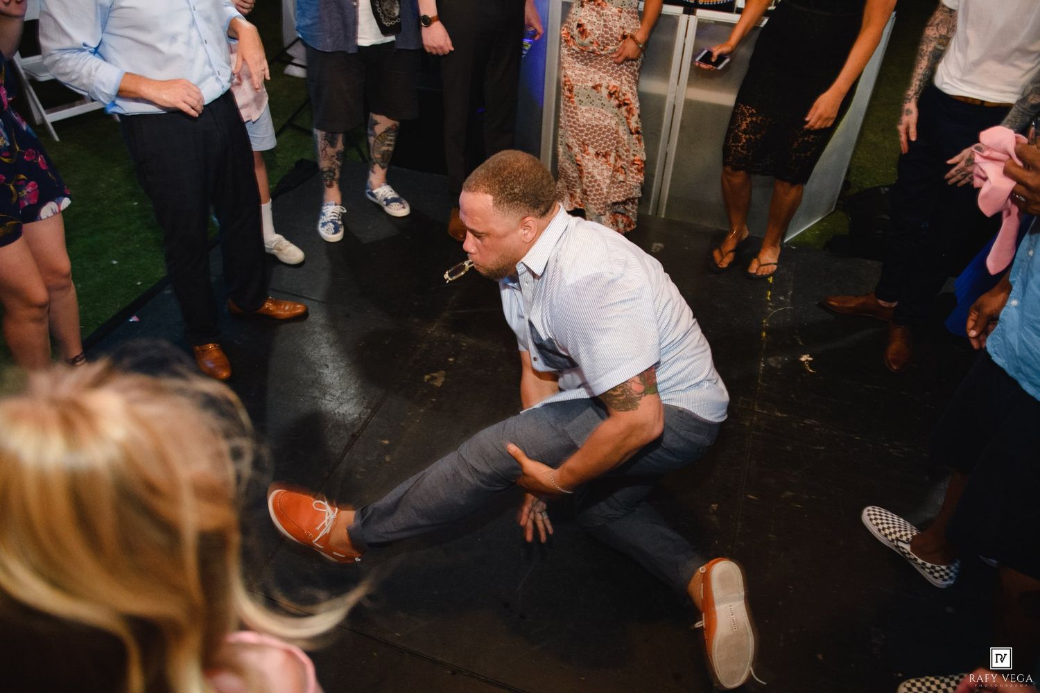Man dancing energetically at a wedding reception, crouching low on the dance floor surrounded by guests.