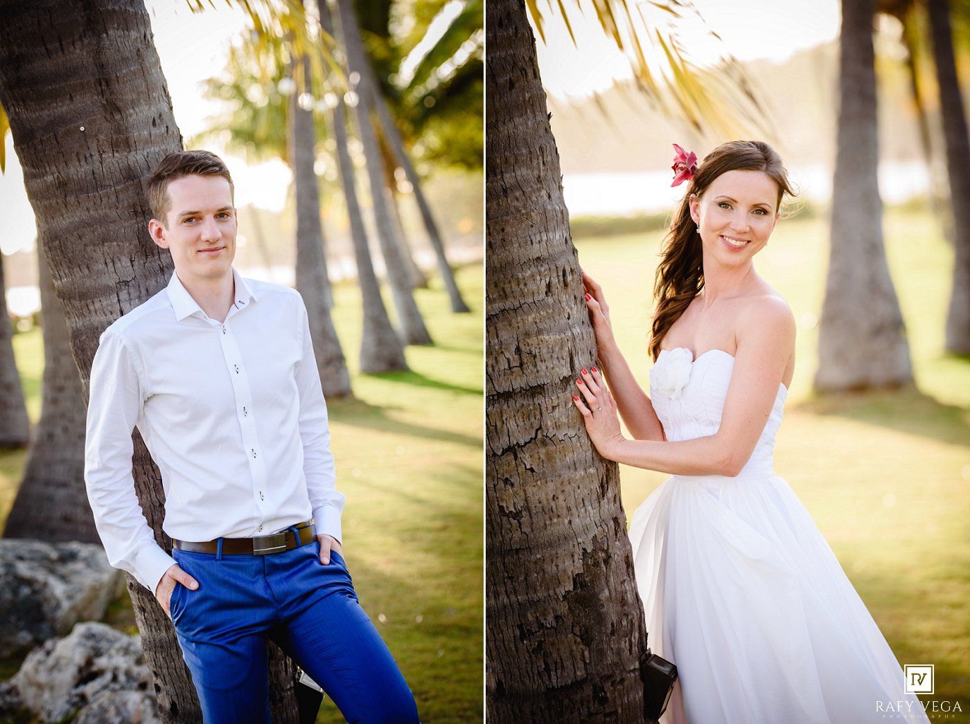 A groom in white shirt and blue pants poses near palm trees beside his bride in a strapless white gown with a floral hair accessory.