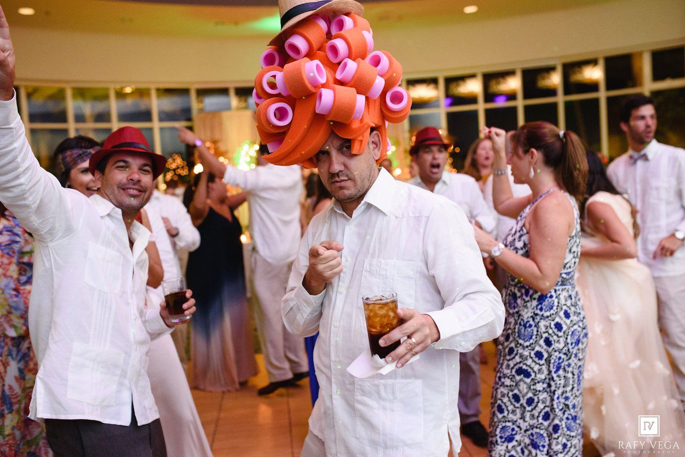 Man dancing in pink hair rollers hat at lively wedding reception party.