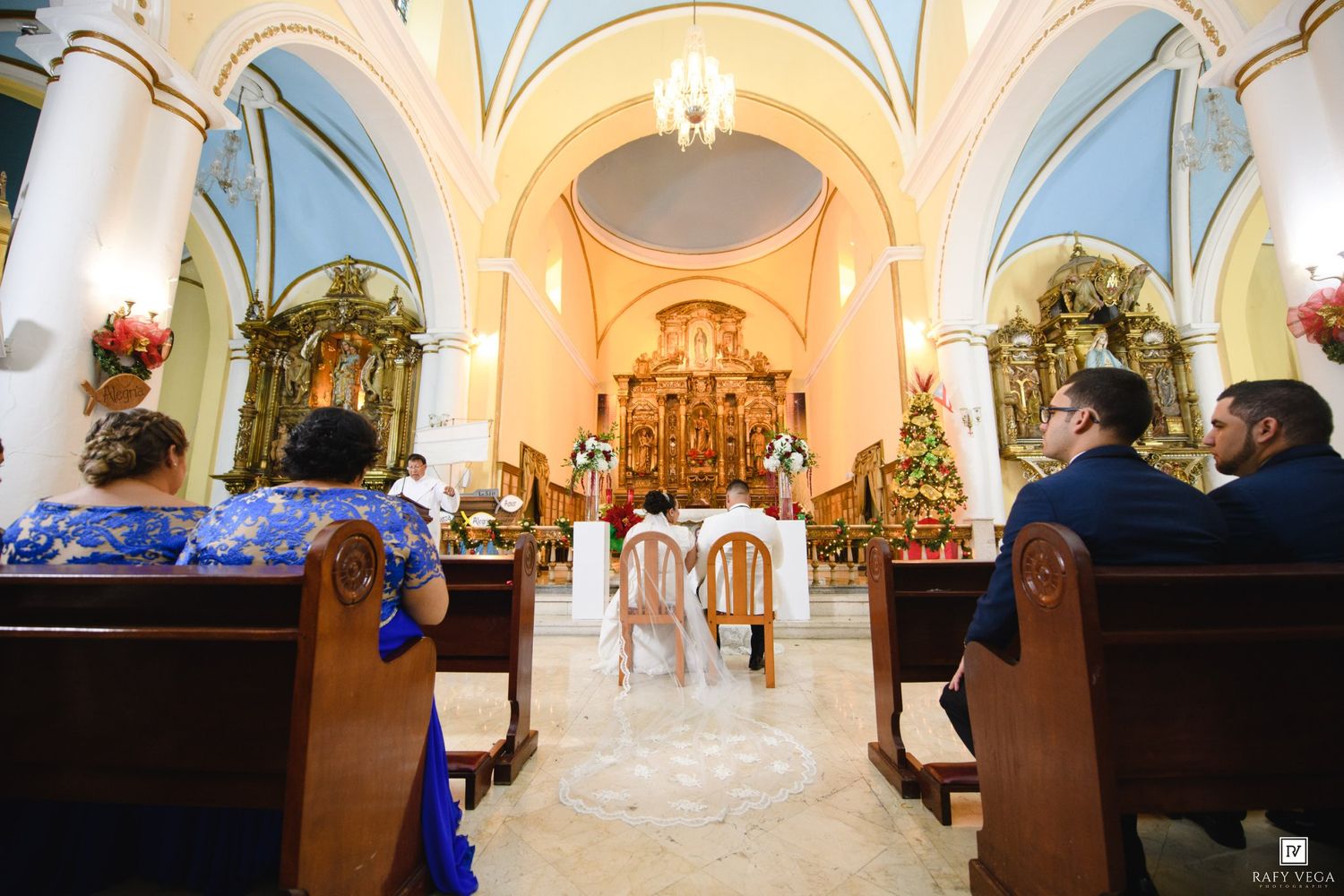 Elegant church wedding ceremony with guests seated in wooden pews facing a ornate golden altar adorned with flowers.