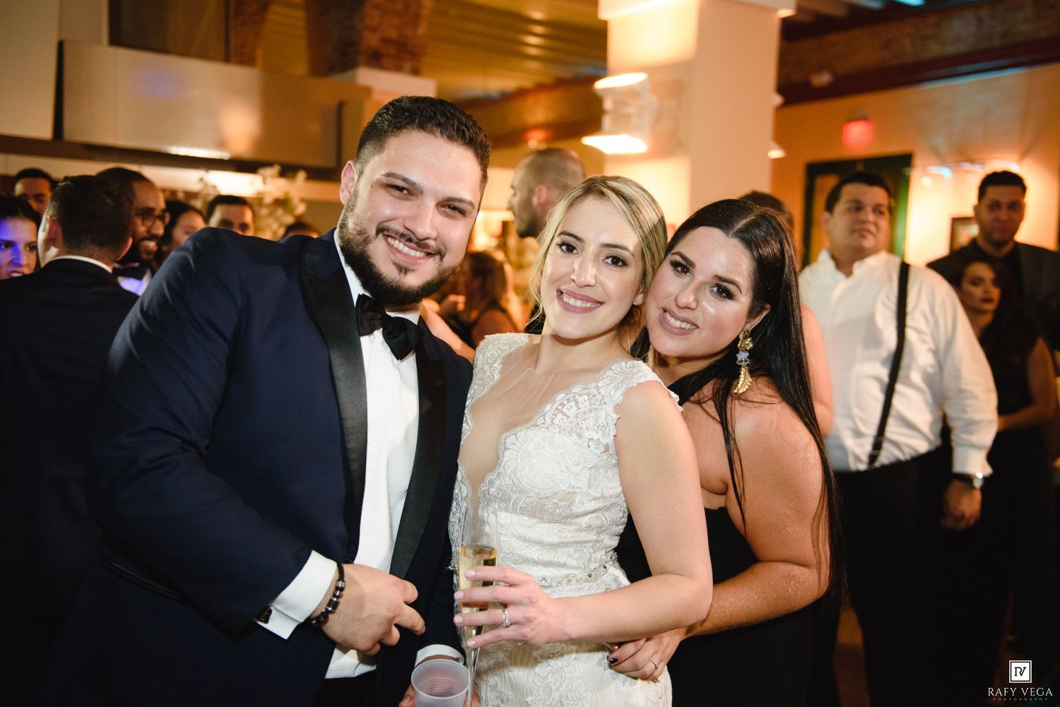 Three elegantly dressed guests smiling together at a formal wedding reception event.