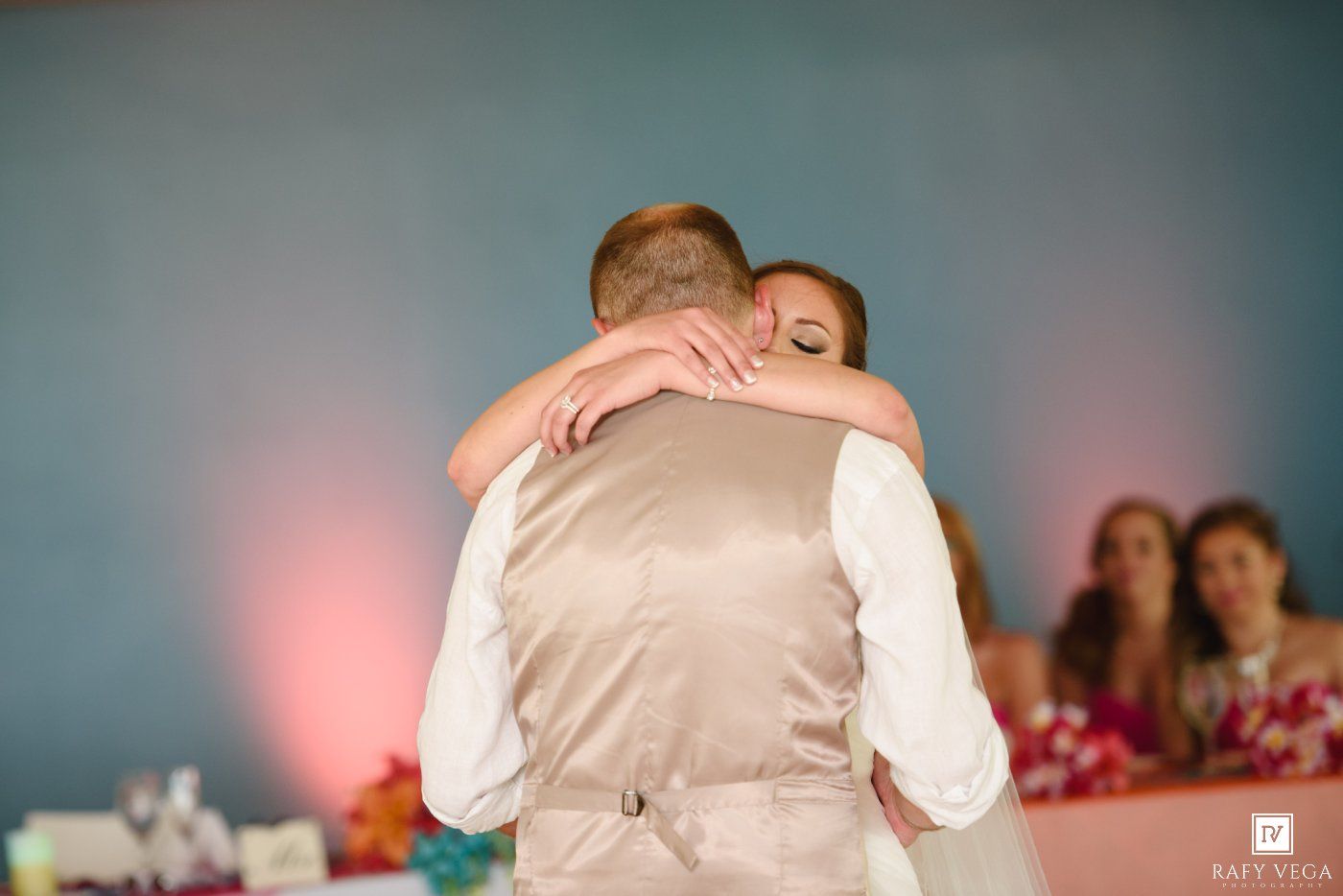 Bride and groom share an emotional first dance hug at their wedding reception with guests watching in background.