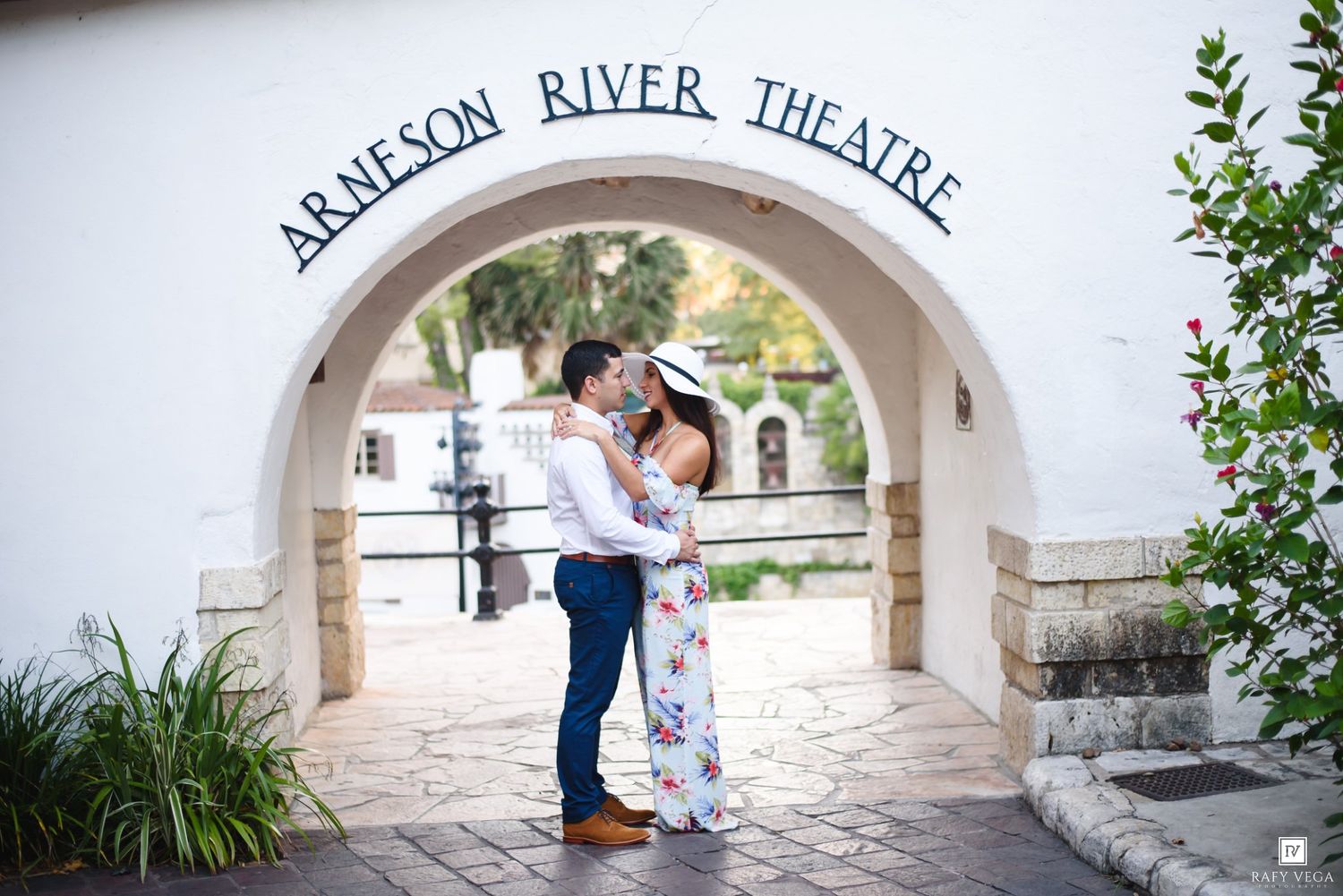 Couple embracing and kissing under the Arneson River Theatre archway outdoors.