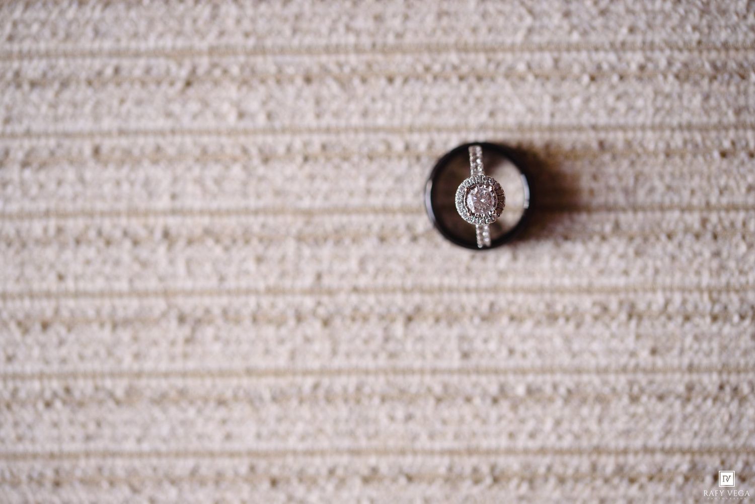 Close-up of a diamond engagement ring and wedding band displayed on a textured cream fabric surface.