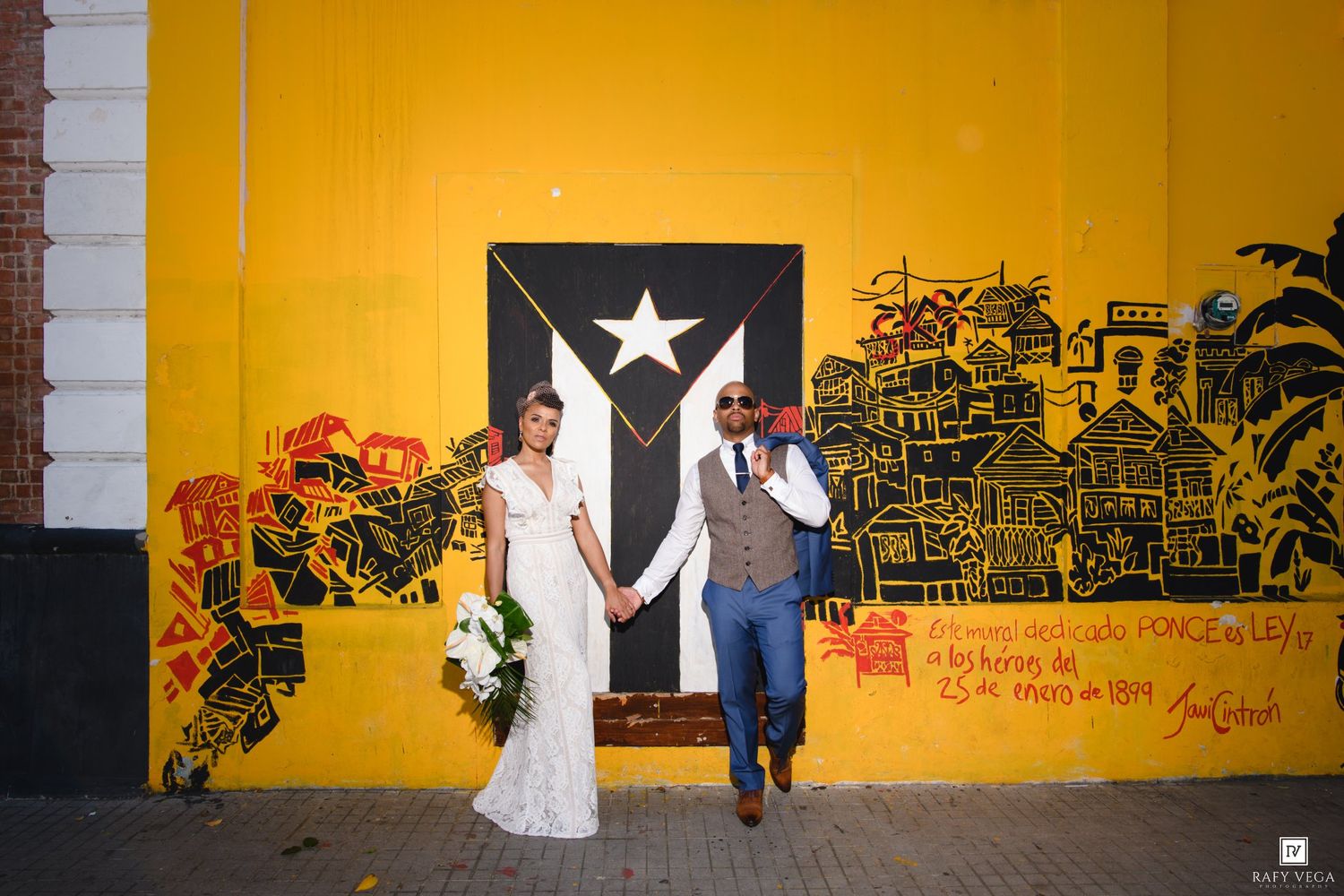 Bride and groom holding hands walking past vibrant yellow Puerto Rico mural street art.