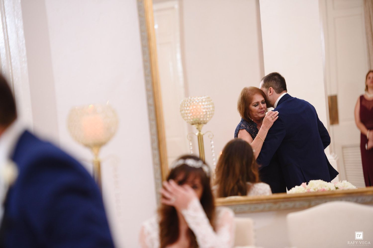 Elegant wedding reception with couple sharing a dance near a ornate mirror and glowing candle centerpiece.