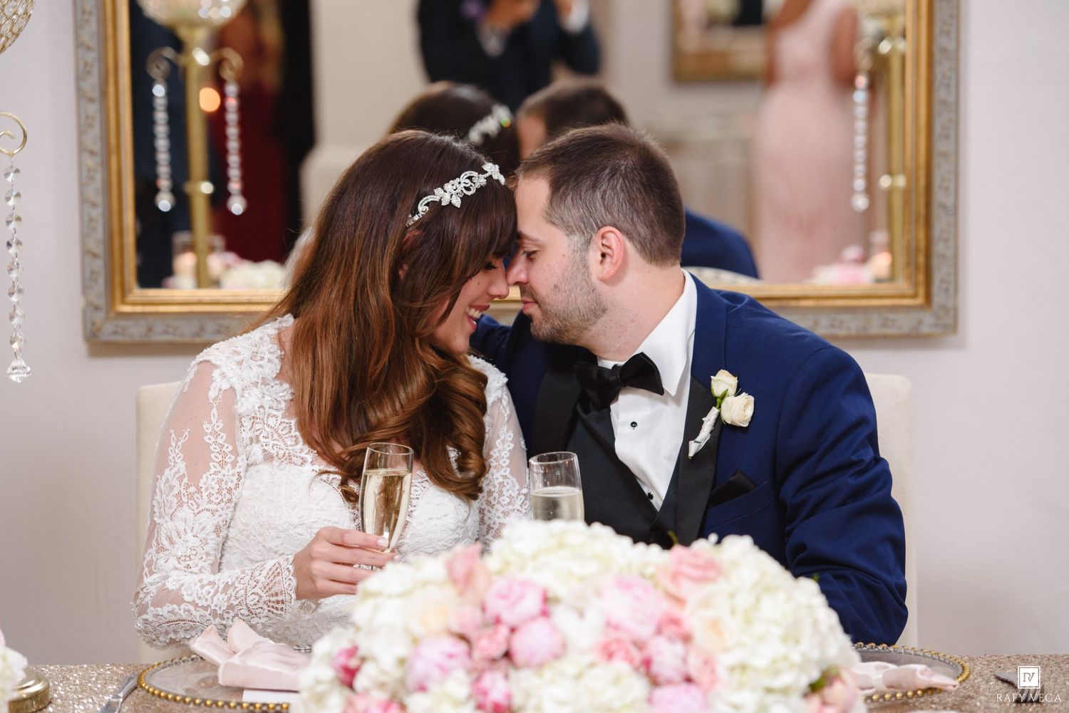 Bride and groom share a romantic moment at sweetheart table with champagne and pink floral centerpiece.