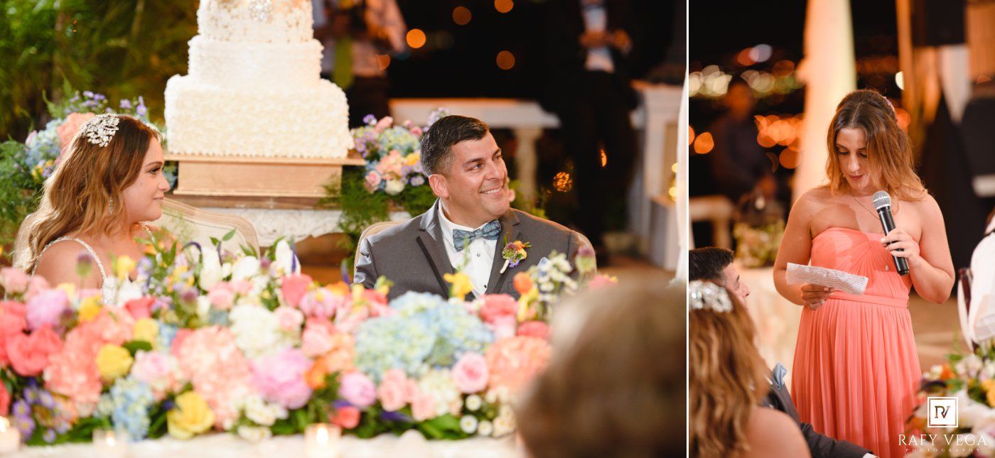 A bridesmaid in coral reads a speech at a wedding reception with floral arrangements and a tiered cake nearby.