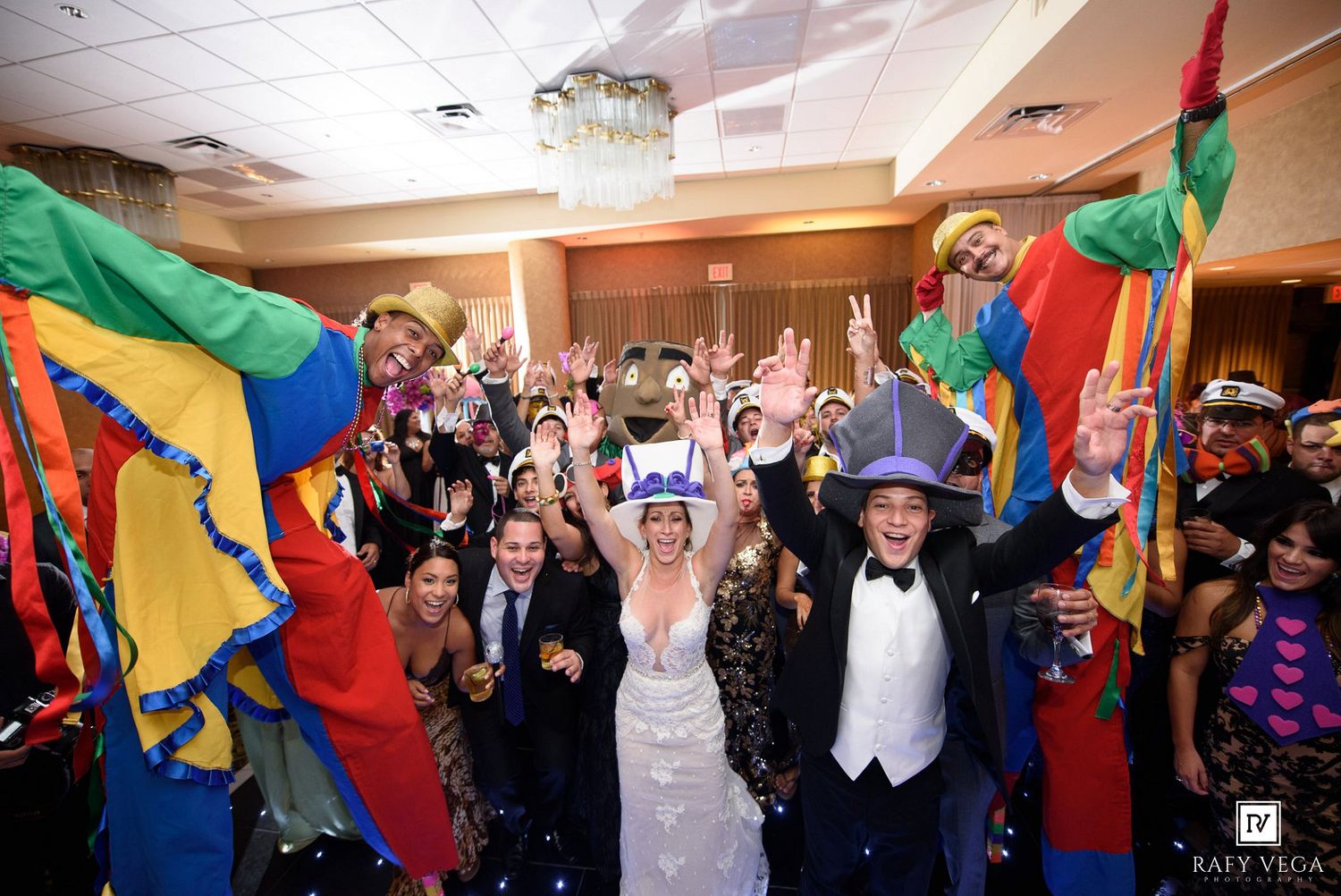 Joyful wedding reception with bride and groom surrounded by colorful confetti, costumes, and celebrating guests in a festive ballroom.