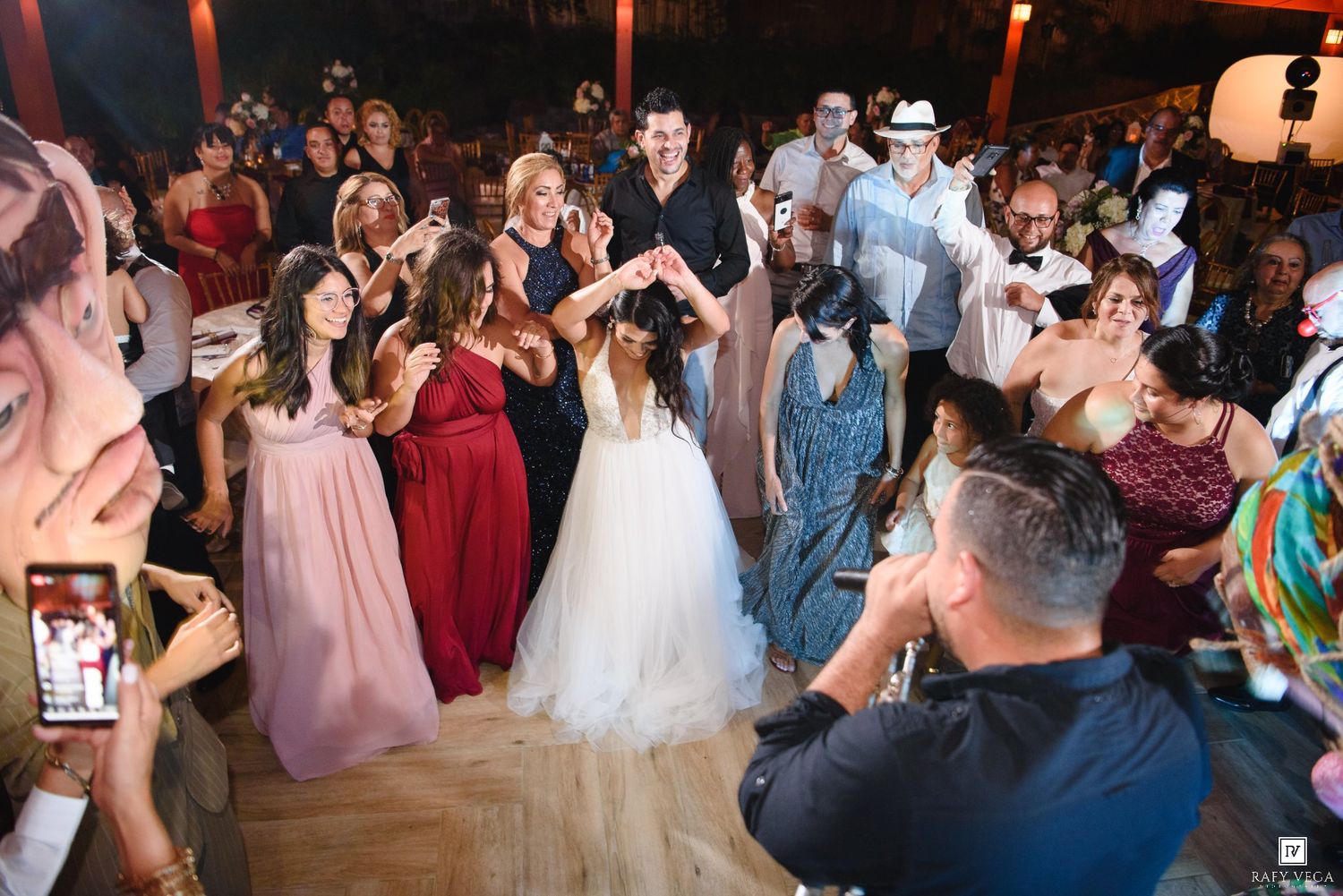 Bride and groom dancing joyfully surrounded by guests in formal attire at a lively wedding reception on the dance floor.