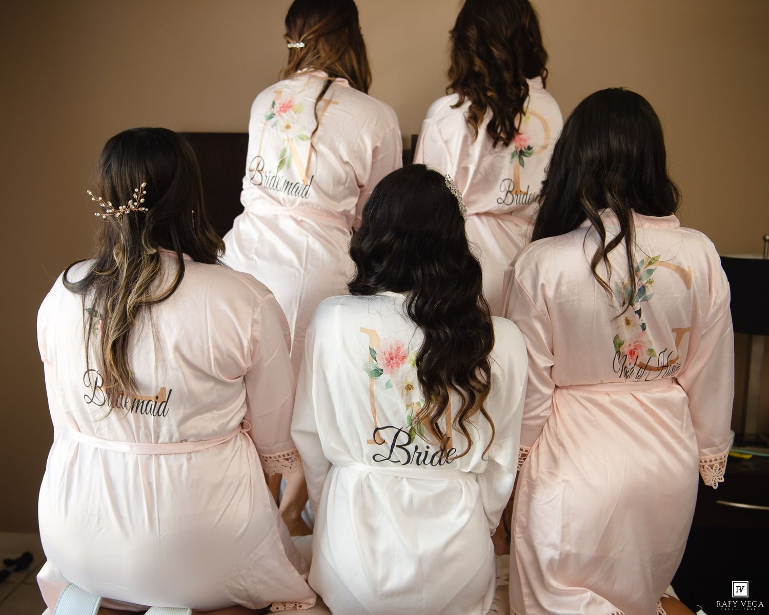 Bridesmaids and bride wearing matching blush pink satin robes with floral embroidery during wedding preparations.