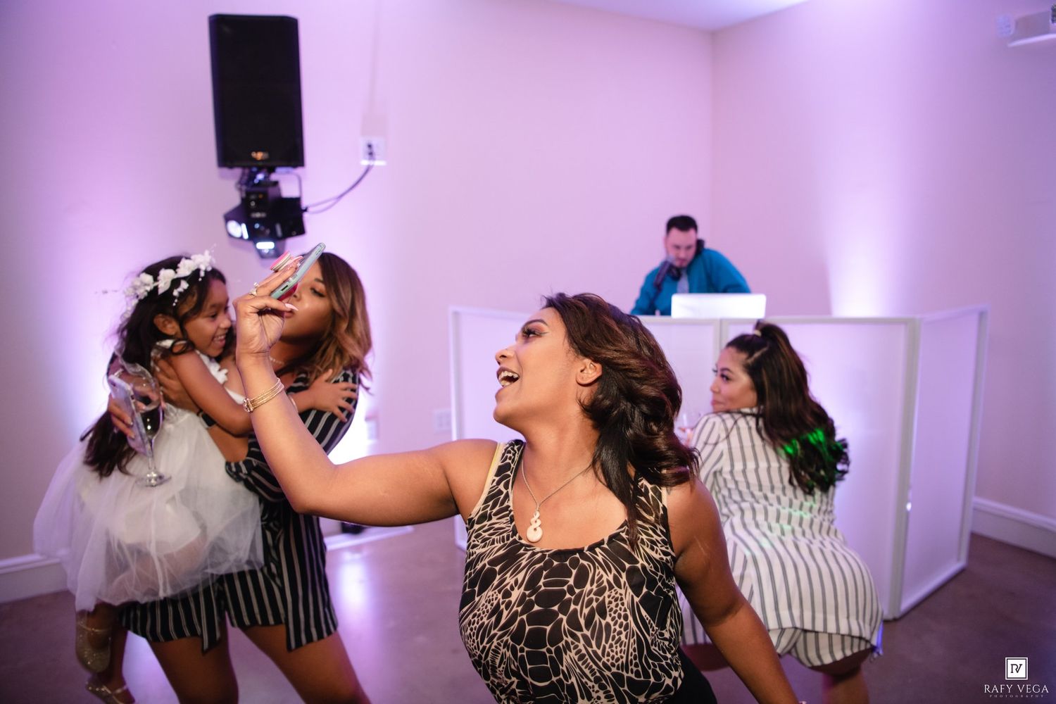 Women dancing and laughing at a wedding reception with a DJ performing in the background.