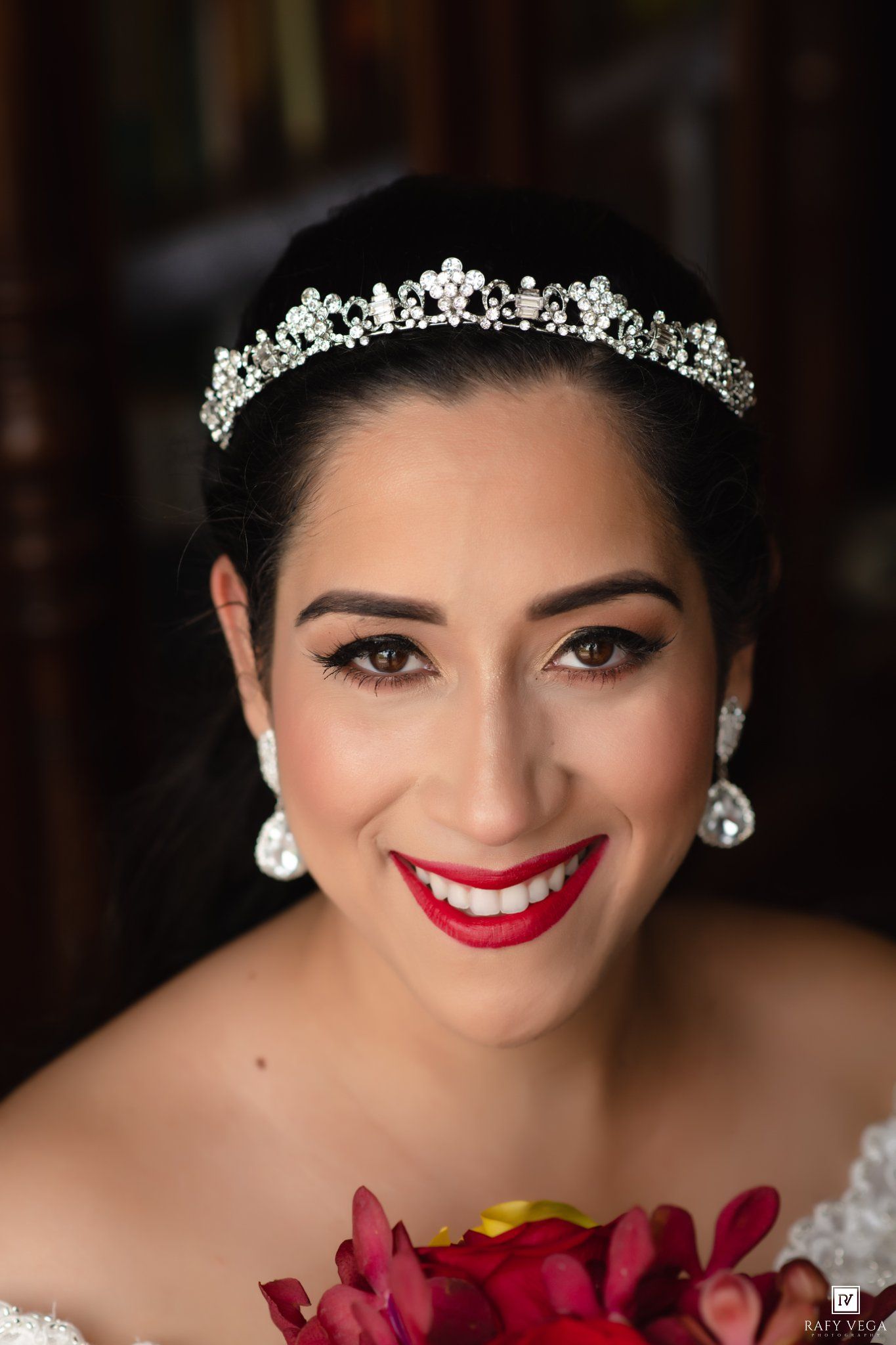 Beautiful bride smiling with red lips, crystal tiara, and drop earrings on her wedding day.