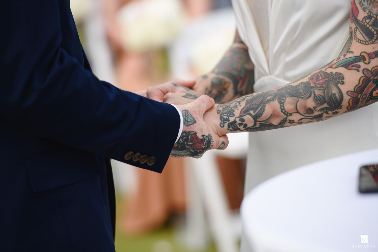 Tattooed groom and bride holding hands during outdoor wedding ceremony, showcasing colorful sleeve tattoos.